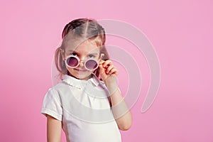 Casual 7 y.o. female in pink round sunglasses isolated on pink background