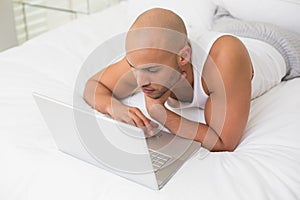 Casual bald man using laptop in bed