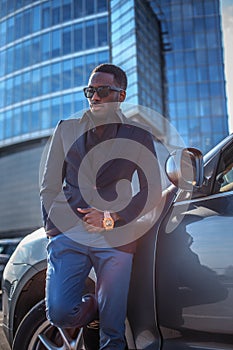 Casual black man in sunglasses posing near car in town.