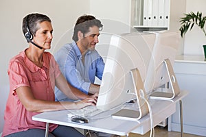 Casual business team working at desk using computers with woman using headset