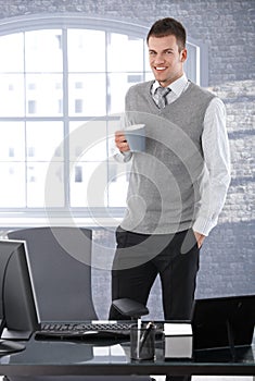 Casual businessman drinking tea in office smiling