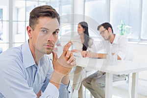 Casual businessman frowing at camera with team behind him photo