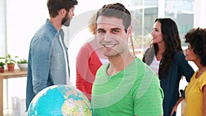 Casual businessman holding terrestrial globe with his colleagues behind