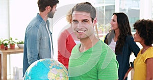 Casual businessman holding terrestrial globe with his colleagues behind