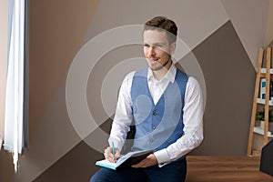 Casual businessman with pen in writing on paper notebook in office in shirt