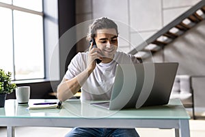 Casual businessman working at office desk, using mobile phone and laptop computer, typing, making phone call