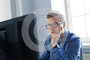 Casual businessman working in office, sitting at desk, typing on keyboard, looking at computer screen.