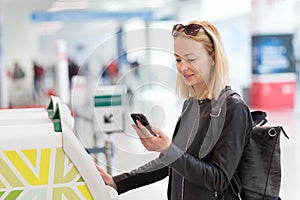 Casual caucasian woman using smart phone application and check-in machine at the airport getting the boarding pass.