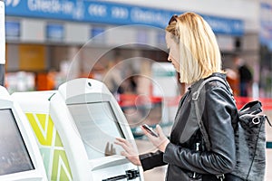 Casual caucasian woman using smart phone application and check-in machine at the airport getting the boarding pass.