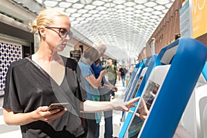 Casual caucasian woman using smart phone application and check-in machine at the airport getting the boarding pass.