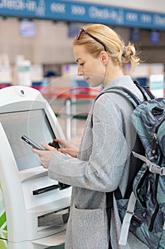 Casual caucasian woman using smart phone application and check-in machine at the airport getting the boarding pass.