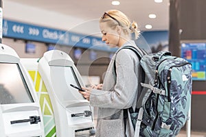 Casual caucasian woman using smart phone application and check-in machine at the airport getting the boarding pass.