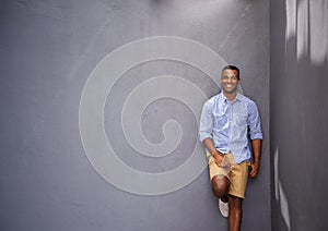 Casual confidence. A handsome young man leaning against a bluegray wall.