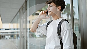 Casual-cool young hispanic university student, using smartphone for an important call with his backpack on, standing in sunlit