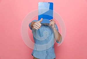 Casual denim guy covering face with clipboard