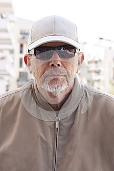 Casual dressed middle age or elderly man with black sunglasses, white cap, wearing windbreaker and a little gray beard