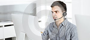 Casual dressed young man using headset and computer while talking with customers online. Call center, business concept