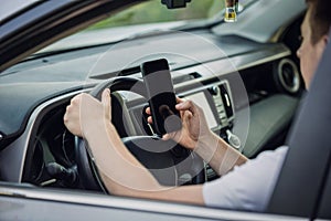 Casual driver guy distracted by his phone while in front of the steering wheel, using his smartphone with one hand while driving.