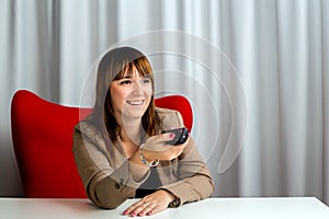 Casual elegant businesswoman at office using TV remote control