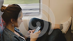 Casual female European daily commuter on the train sits comfortable near window using smartphone book reading app.