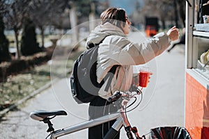 Casual girl ordering food at a park kiosk with her bicycle