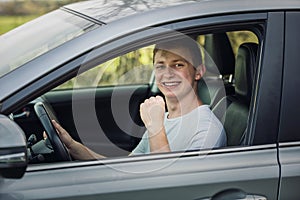 Casual guy keeps fist up tight looking out of the driver window of his new car. Successful young man bought a new car, celebrating