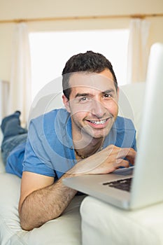 Casual happy man sitting on couch using laptop looking at camera