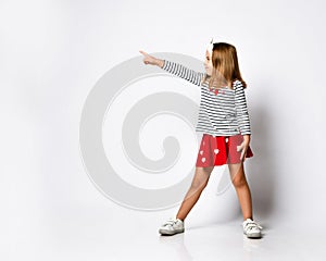 Casual little girl in a red skirt pointing and looking to her side with a smile.
