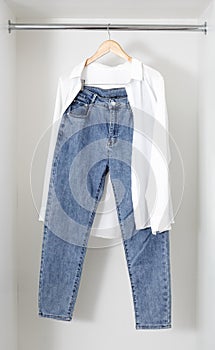 Casual look with white blouse and blue jeans hanging on wooden hanger on white background