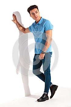 Casual man in blue polo shirt, leaning against studio wall