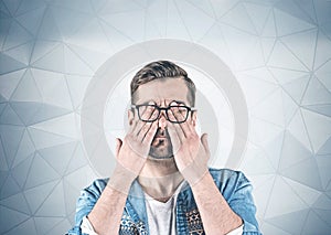 Casual man covering eyes with hands, gray wall