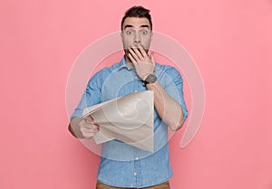 Casual man covering mouth, schocked by news from newspaper