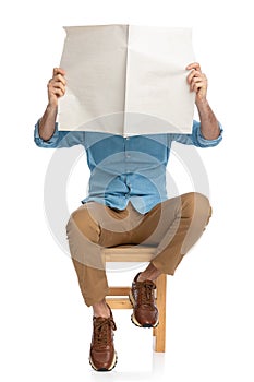 Casual man in denim shirt covering face with newspaper