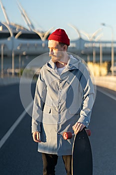 Casual man with longboard over city building. Hipster stylish skateboarder hold skateboard on sunset