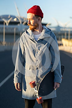 Casual man with longboard over city building. Hipster stylish skateboarder hold skateboard on sunset