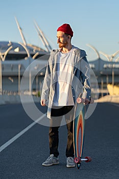 Casual man with longboard over city building. Hipster stylish skateboarder hold skateboard on sunset