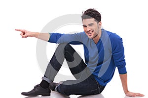 Casual man is pointing to his side while sitting