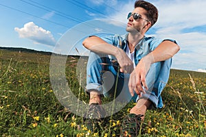 Casual man resting on a field outside looks to side