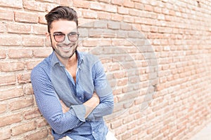 Casual man resting near brick wall with hands crossed