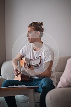 Casual man sits on the sofa, strumming the village rag. He is letting his artistic side flow. The singer strums his guitar while