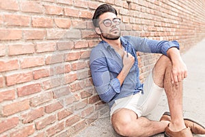 Casual man sitting near brick wall looking up