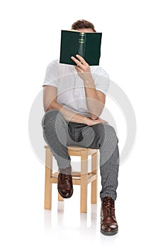 Casual man sitting and reading a book covering his face