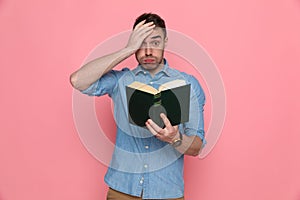 Casual man slapping his head, holding his book