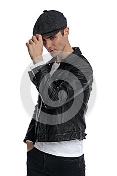 Casual man standing with hand in pocket fixing hat tough