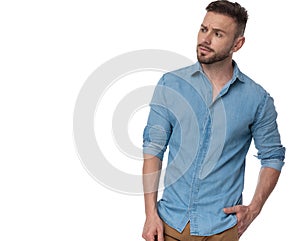 Casual man standing with hand in pocket looking sideways intrigued