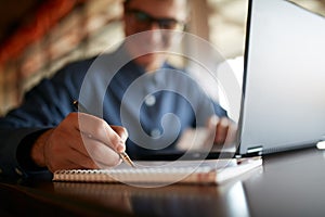 Close-up of smiling man hand writing on paper notebook. Young businessman in glasses taking notes in notepad with