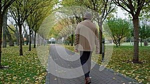Casual man walking slowly through park in autumn weather. Mature senior going .