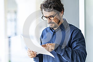 Casual man wearing glasses  reading paper document or contract.