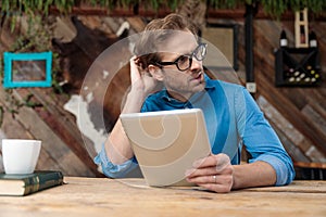 Casual man holding his tablet while scratching head pensive