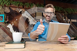 Casual man working on tablet while giving a thumbs up